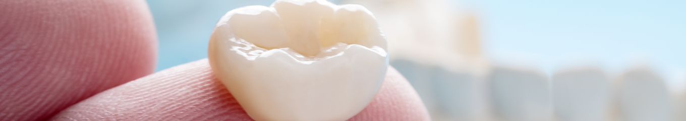 Close up of a dental crown resting on a person's finger