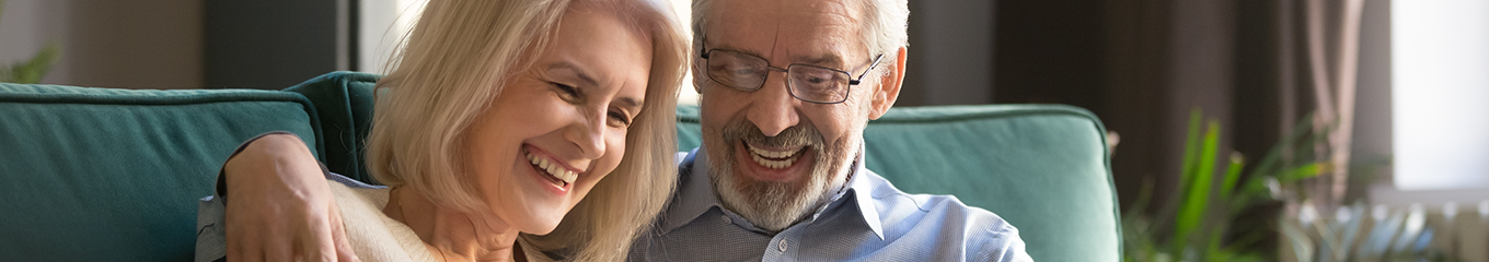 Senior man and woman smiling on a couch while looking at a tablet