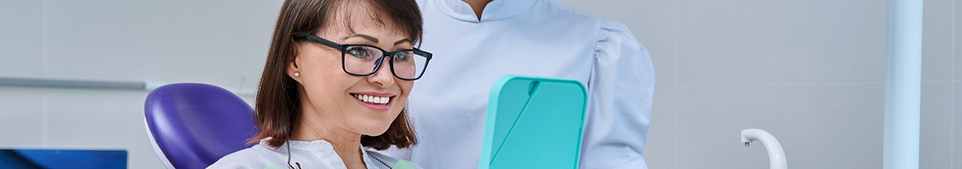 Dental patient looking at her new and improved smile in a mirror